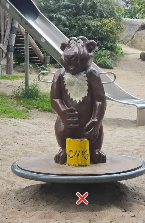 Hölzerner Bär auf einem Spielplatz-Karussell, daneben eine Rutsche