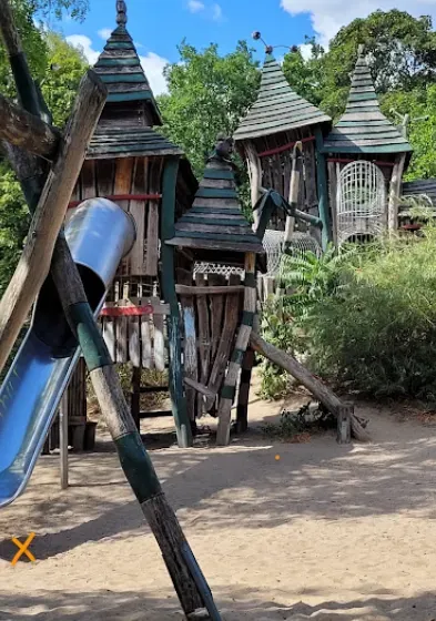 Hölzerne Spielburg mit Türmen und einer Röhrenrutsche auf einem Spielplatz